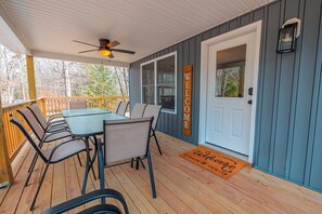 A covered porch with a table and chairs, a ceiling fan, a welcome sign, and a door with a doormat. - NEW Large Group Summer Getaway W/hot Tub + Game Room! (Albrightsville)
