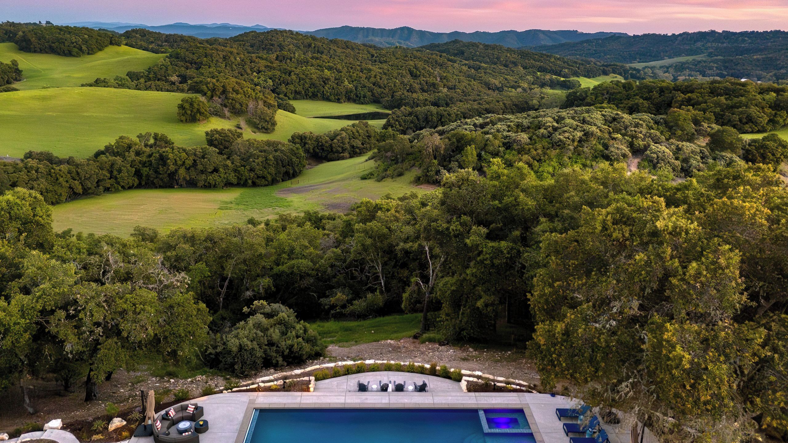 A pool with lounge chairs, surrounded by lush greenery and hills.