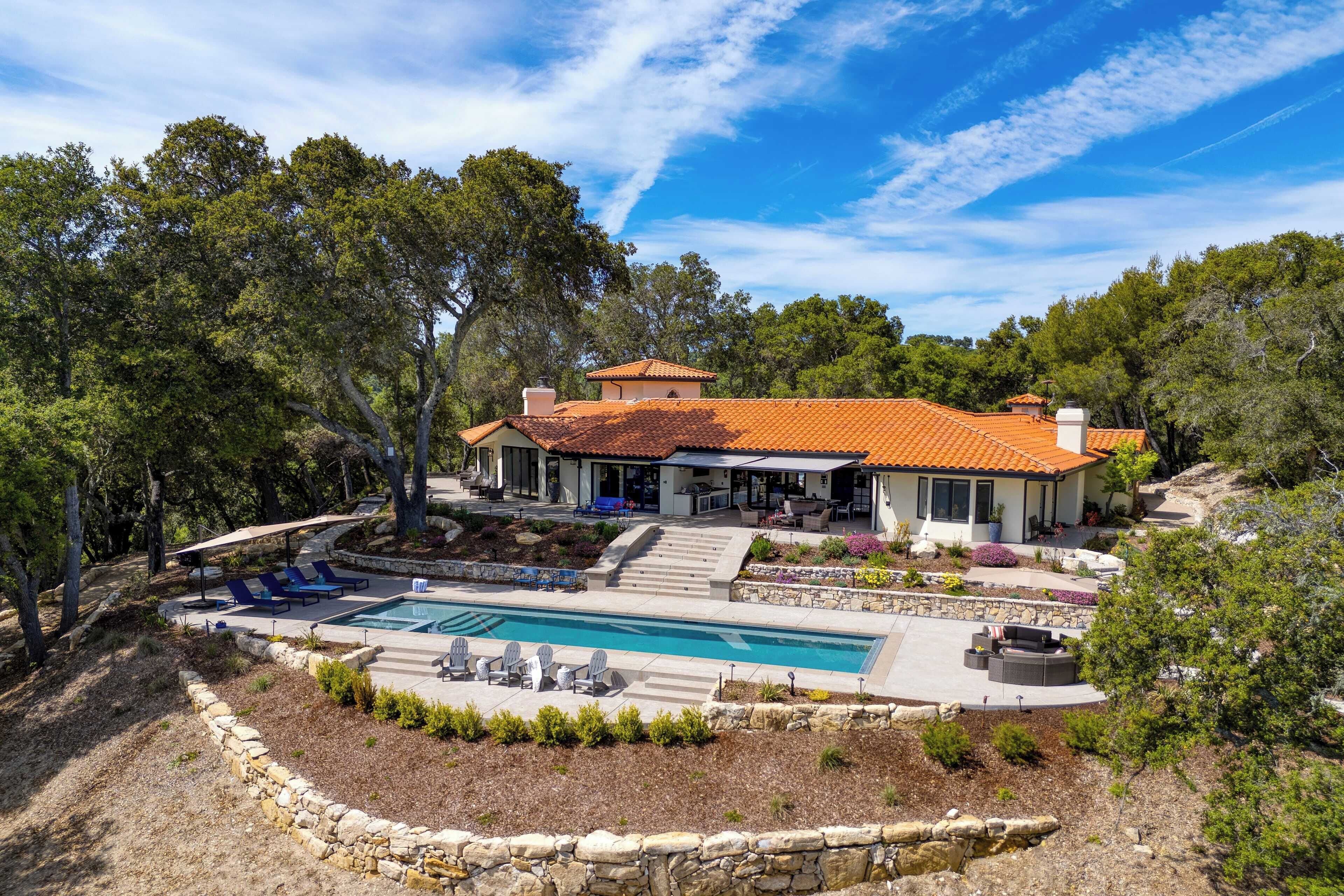 A house with a swimming pool, outdoor seating, and a stone retaining wall.