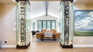 A modern living room with a glass wine rack, a sofa, and a painting on the wall. - Rancho Robles by Avantstay Vineyard Villa w/ Views, Pool & Privacy (Paso Robles)