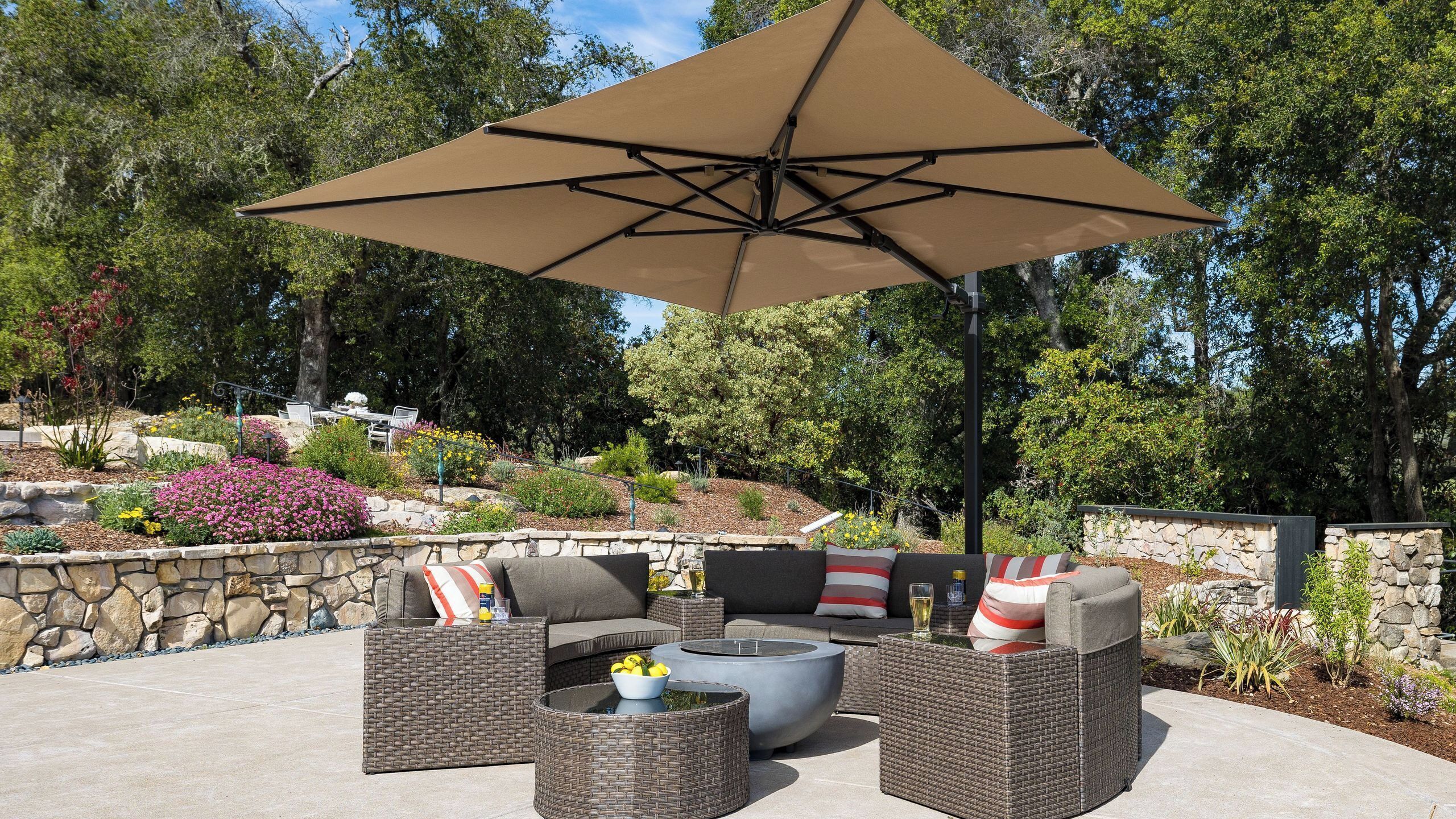 An outdoor patio with wicker furniture, a stone wall, and a large umbrella.