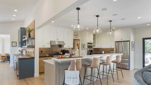 A modern kitchen with a central island, bar stools, and pendant lighting. - Rancho Robles by Avantstay Vineyard Villa w/ Views, Pool & Privacy (Paso Robles)