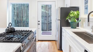 A modern kitchen with a gas stove, stainless steel appliances, a large window with a view of bamboo, and a potted plant on the counter. - A-lister by Avantstay Hollywood Hills Luxe Group Escape w/ Pool (Los Angeles)