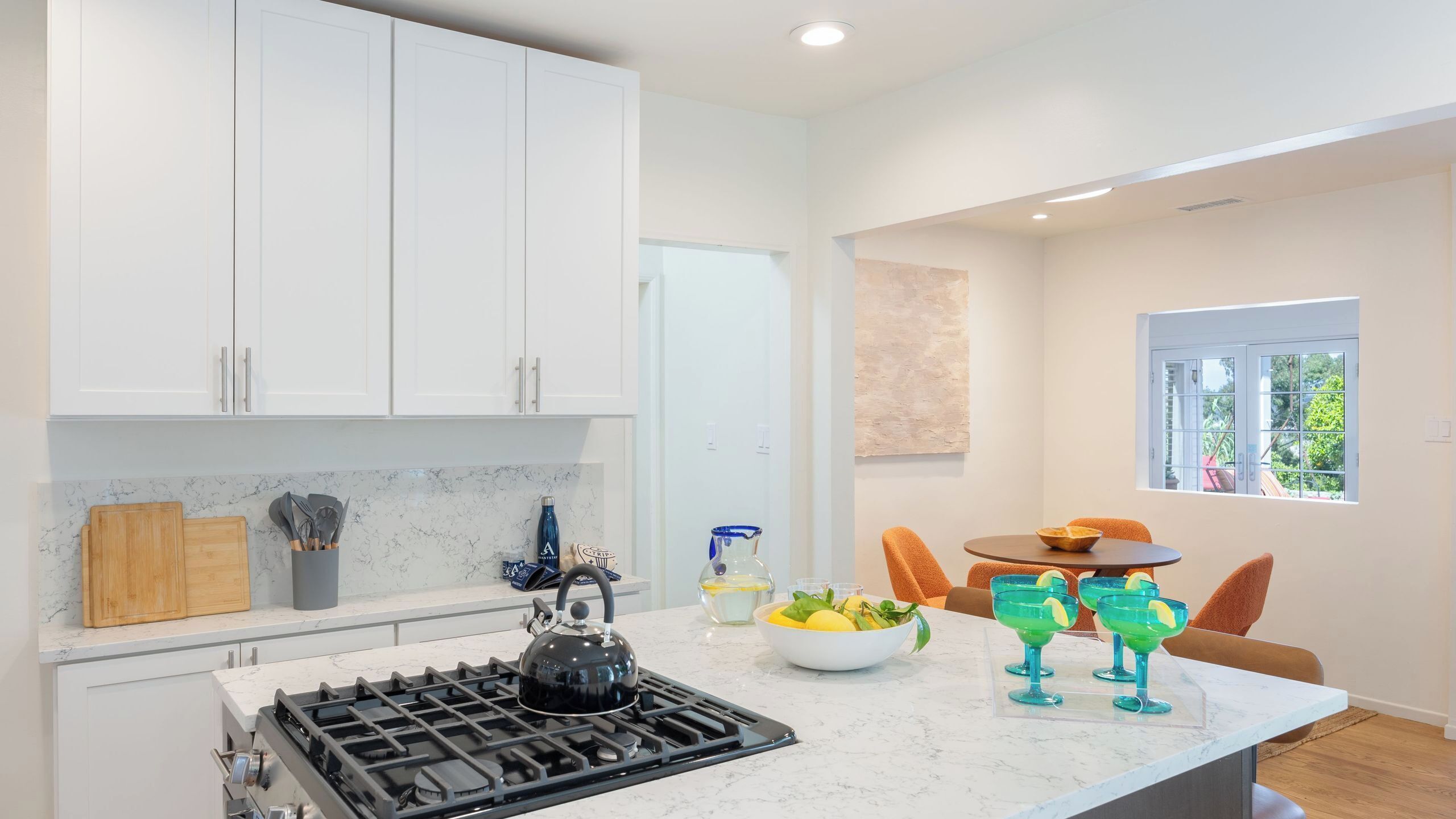 A modern kitchen with white cabinets, a gas stove, and a dining area with a table and chairs.
