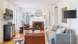 A living room with a fireplace, a sofa, a chair, a TV, and a floor lamp. - A-lister by Avantstay Hollywood Hills Luxe Group Escape w/ Pool (Los Angeles)
