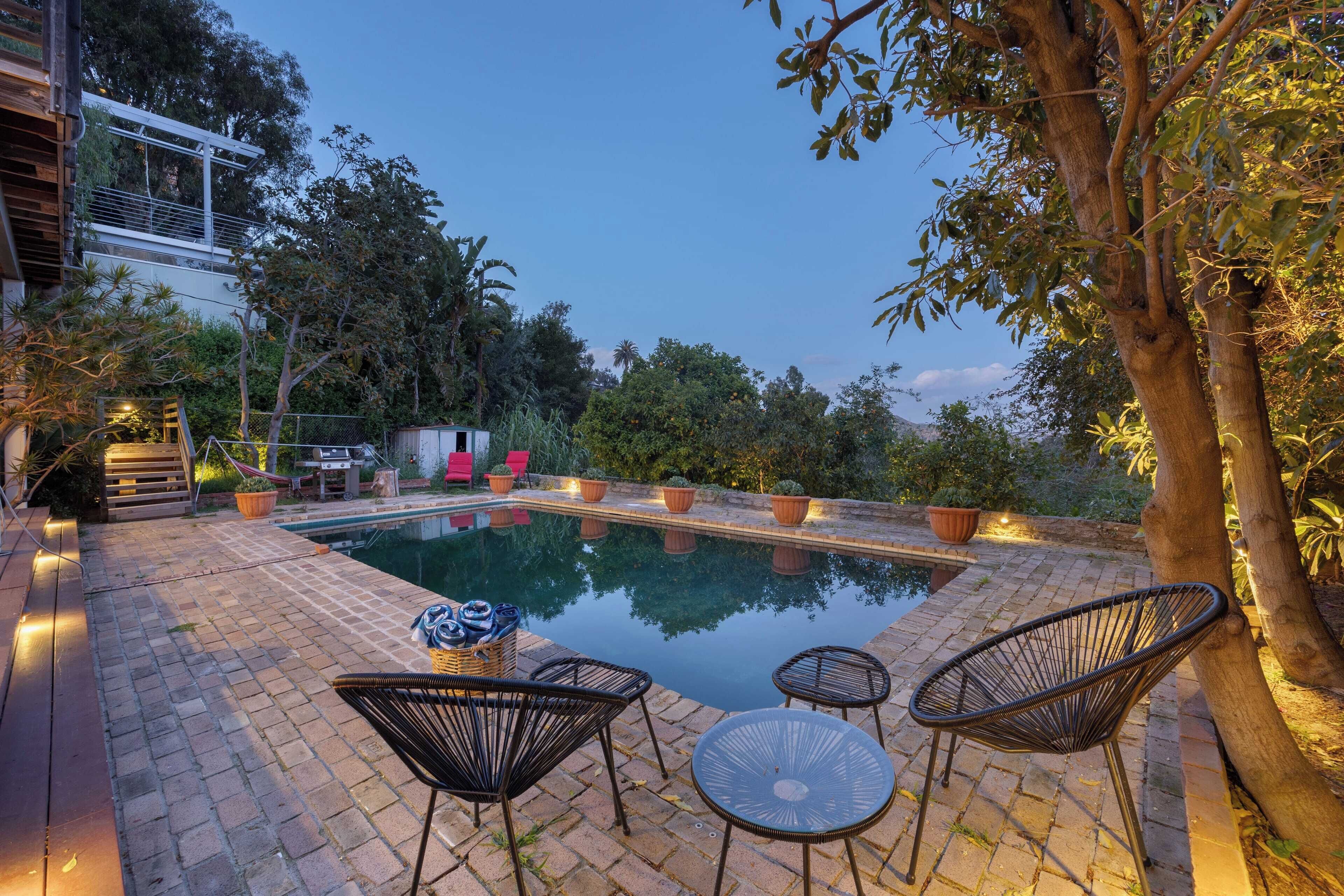 A pool area with a brick patio, lounge chairs, and potted plants.