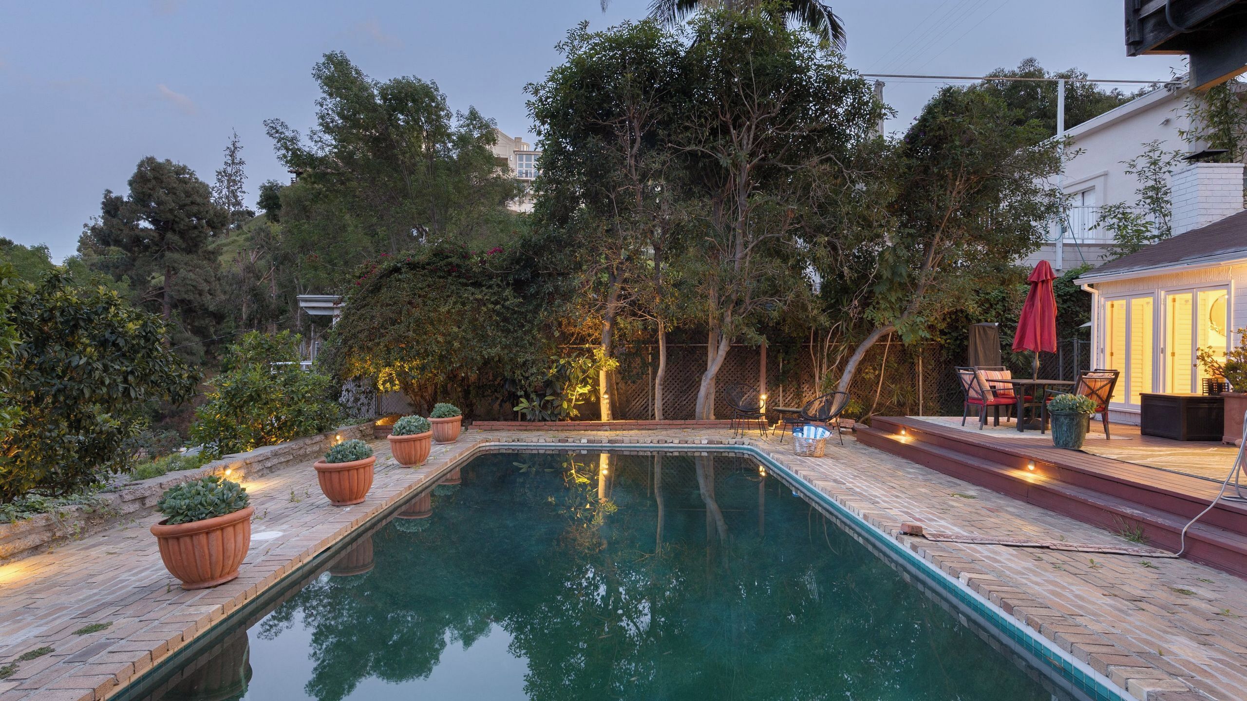 A swimming pool with a brick deck, surrounded by potted plants and trees.