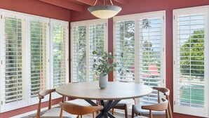 A dining area with a round table, four chairs, a vase with plants, and large windows with blinds. - A-lister by Avantstay Hollywood Hills Luxe Group Escape w/ Pool (Los Angeles)