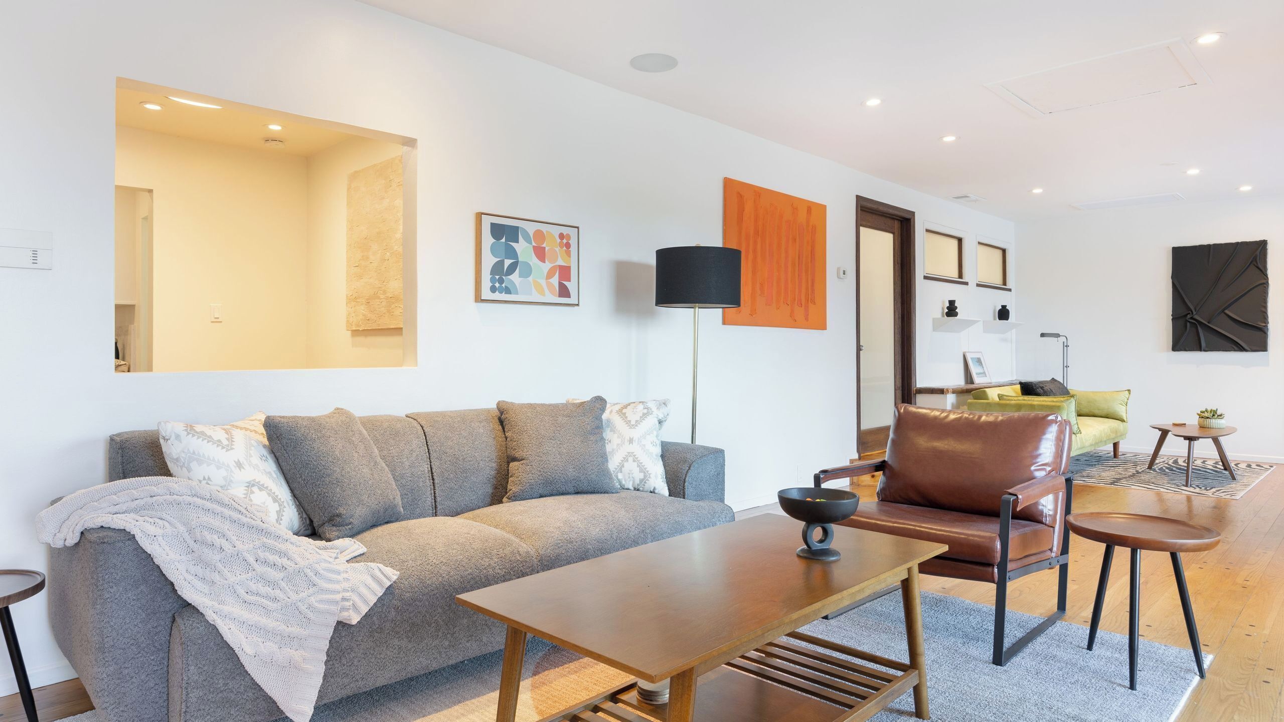 Ein modernes Wohnzimmer mit einem grauen Sofa, einem Holztisch, einem braunen Ledersessel und einer Stehlampe.