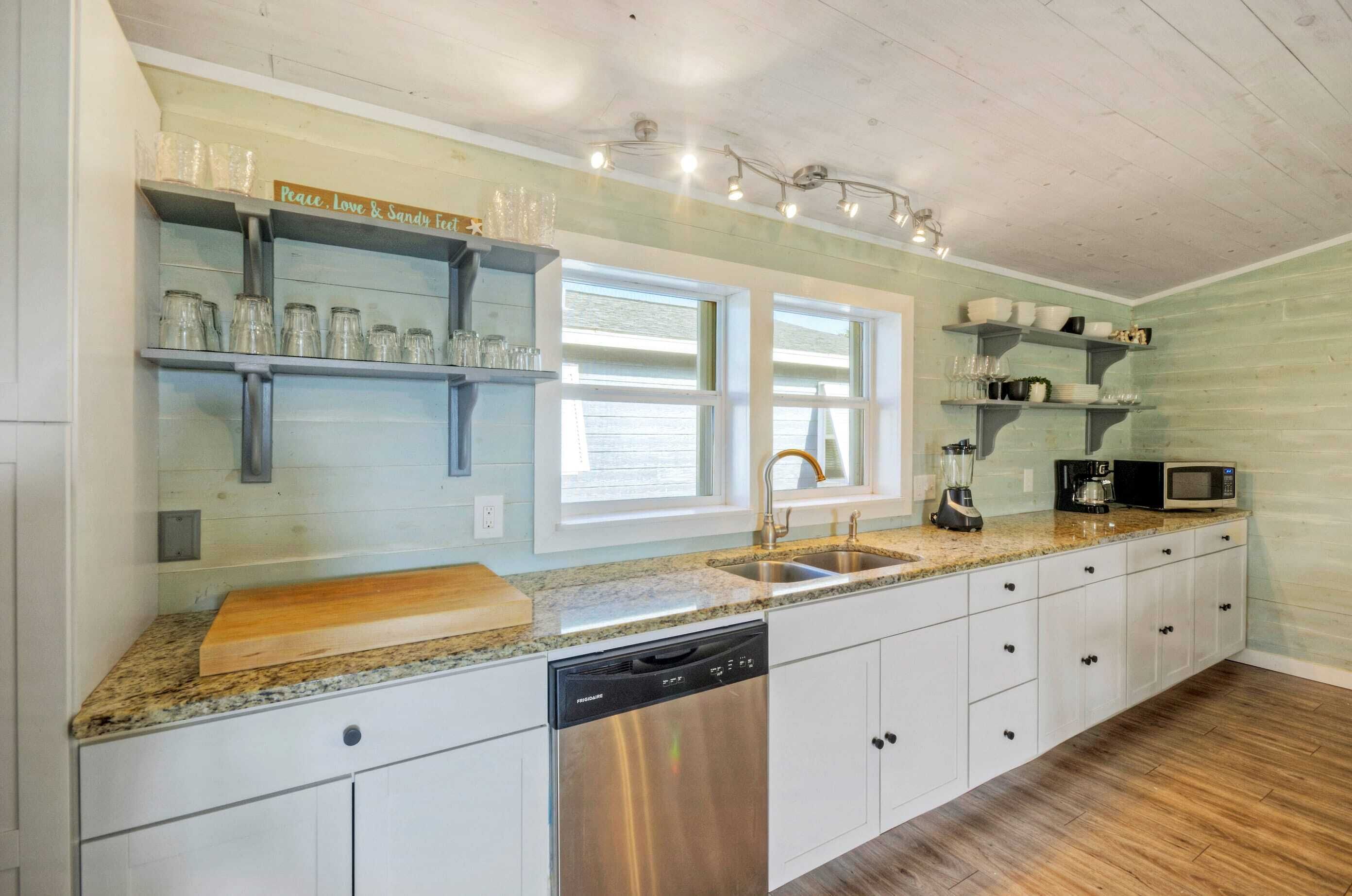 A kitchen with white cabinets, a granite countertop, a dishwasher, a coffee maker, and a microwave.