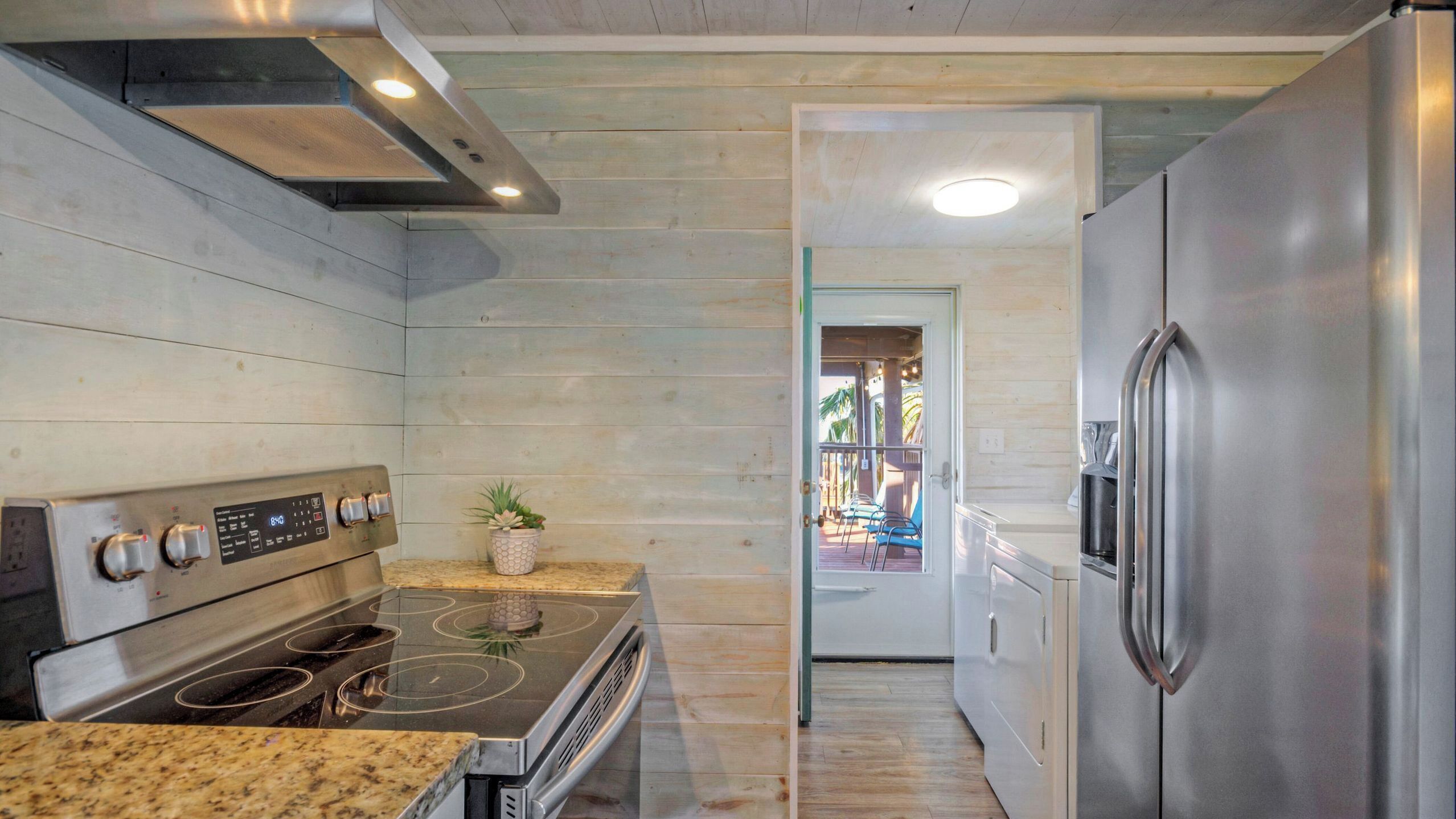 A modern kitchen with stainless steel appliances, a granite countertop, and a potted plant.