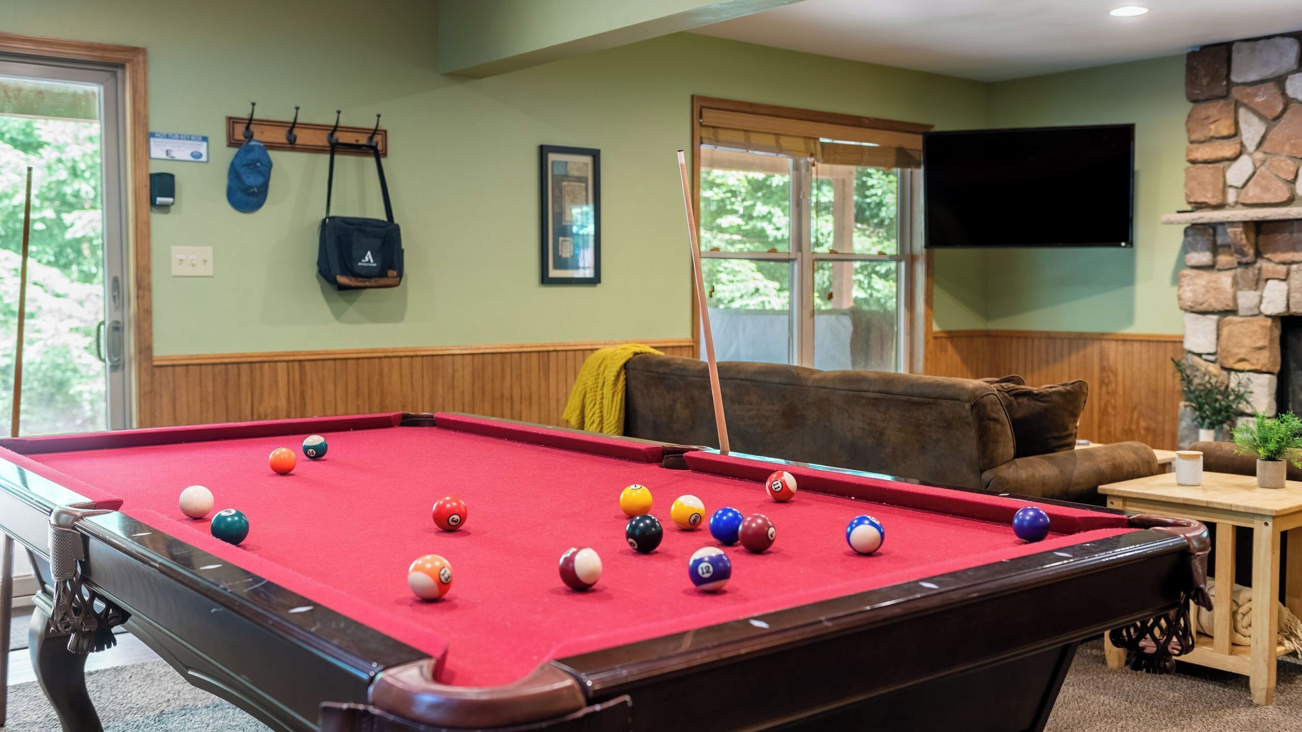 A pool table with balls, a sofa, a television, and a stone fireplace.