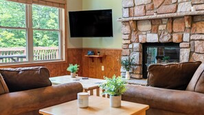 A living room with a stone fireplace, a flat-screen TV mounted above it, and a wooden table with two potted plants.