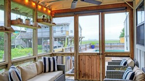 A covered outdoor area with a sofa, cushions, and a view of a house and pool. - Simpatico by Avantstay Pool, Near Birding Center (Port Aransas)