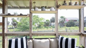 A wooden structure with multiple windows, a cushioned seating area with striped pillows, and various potted plants. - Simpatico by Avantstay Pool, Near Birding Center (Port Aransas)