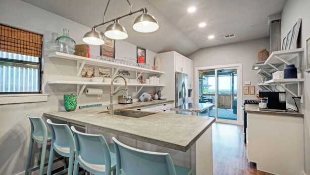 A modern kitchen with a central island, bar stools, and a view to the outside. - Simpatico by Avantstay Pool, Near Birding Center (Port Aransas)