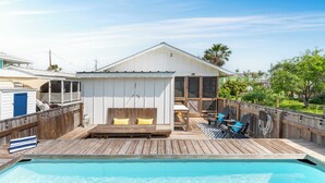 A poolside deck with a wooden deck, a pool, a covered seating area with cushions, and a view of the surrounding neighborhood. - Simpatico by Avantstay Pool, Near Birding Center (Port Aransas)