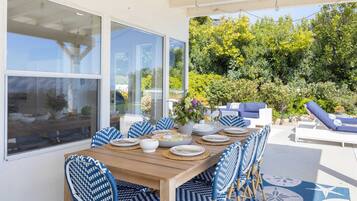 Un área de comedor al aire libre techada con una mesa de madera dispuesta para cuatro personas, rodeada de sillas con estampado azul y blanco.