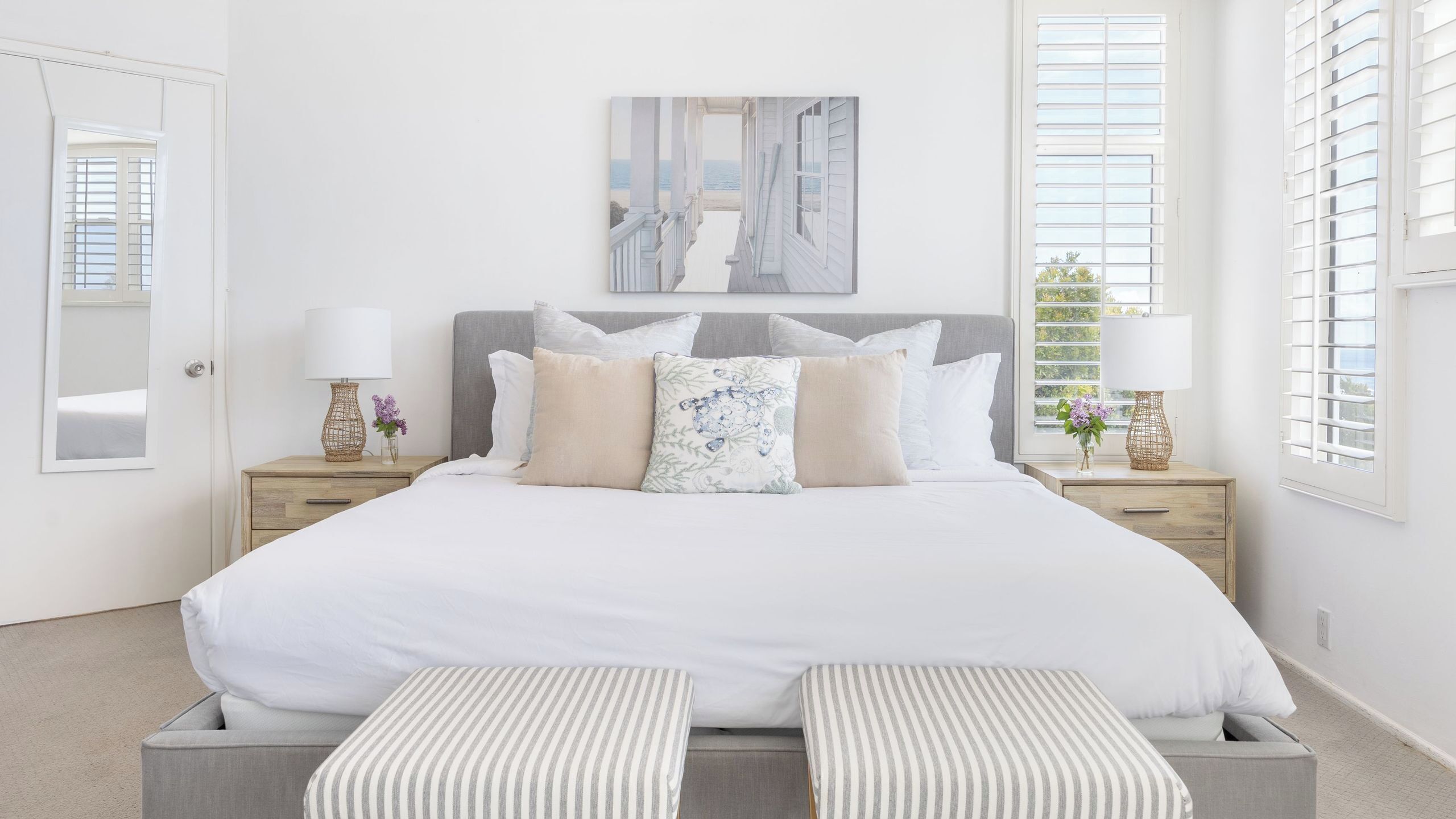 A bedroom with a large bed, bedside tables, a mirror, and a view of the beach.