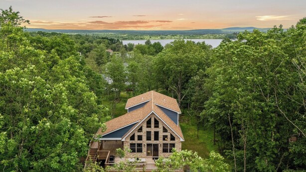 A house with a stone facade, a gabled roof, and a view of a lake surrounded by trees. - Bluejay Getaway by Avantstay Private Lake Cabin Hot Tub + Game Room Walk to Lake (Albrightsville)