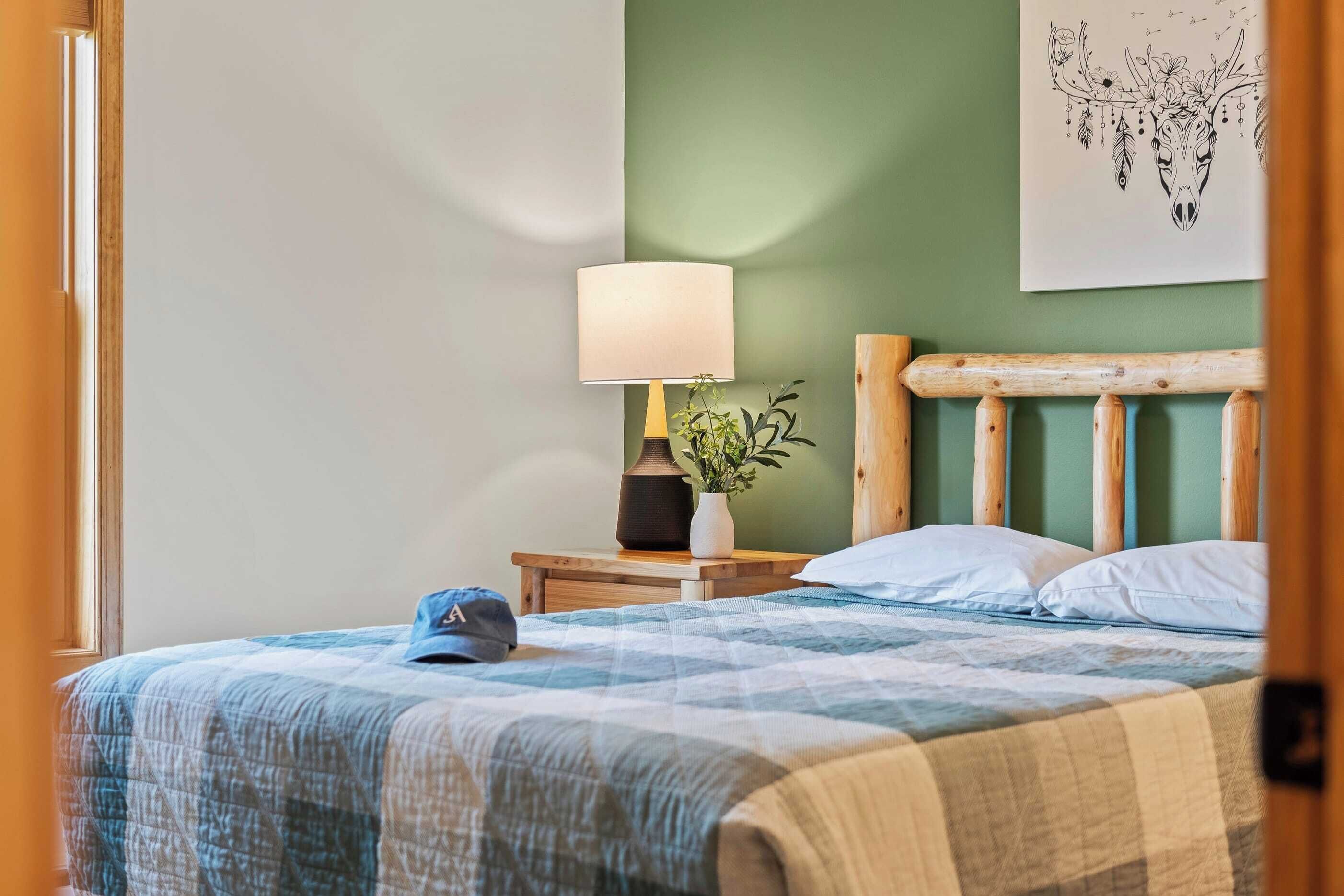 A neatly made bed with a blue and white checkered bedspread, a wooden headboard, a bedside lamp, and a small potted plant on a nightstand.