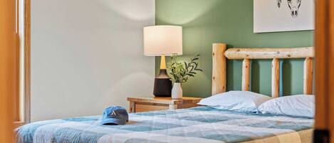 A neatly made bed with a blue and white checkered bedspread, a wooden headboard, a bedside lamp, and a small potted plant on a nightstand.
