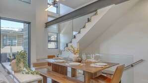 A modern dining area with a long wooden table set for four, benches, and a staircase with a glass railing. - The Ridge at Canyons Village by Avantstay Stunning Slope-side Condo w/ Hot Tub (Park City)