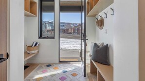 A modern interior with a sliding glass door leading to a snowy outdoor area, wooden shelves, a bench, and a patterned rug. - The Ridge at Canyons Village by Avantstay Stunning Slope-side Condo w/ Hot Tub (Park City)
