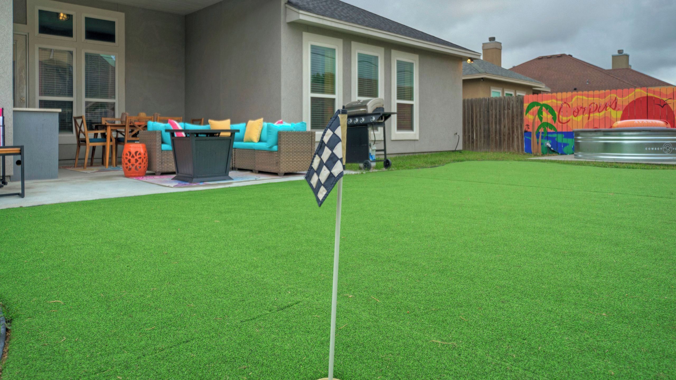 Un patio trasero con césped artificial, una bandera a cuadros y una zona de estar al aire libre con mobiliario.