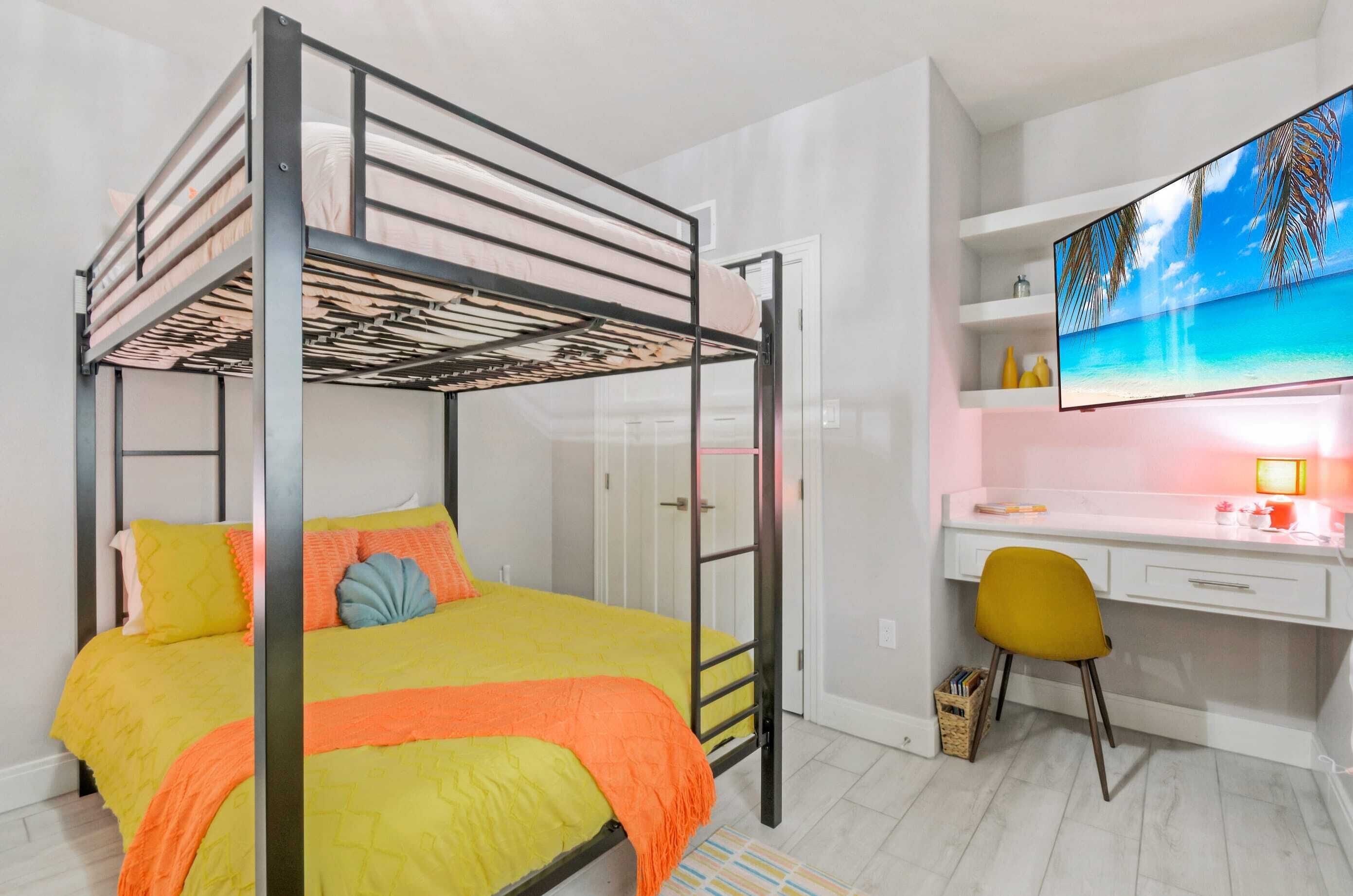A bunk bed with a desk and chair, a TV, and a shelf with decorative items.
