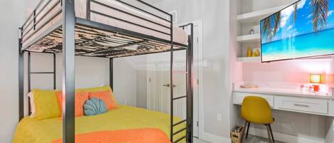 A bunk bed with a desk and chair, a TV, and a shelf with decorative items.