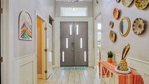 A hallway with a double door, a colorful abstract painting, and woven wall decorations. - Graford by Avantstay Hot Tub, Firepit, Mini Putt (Corpus Christi)