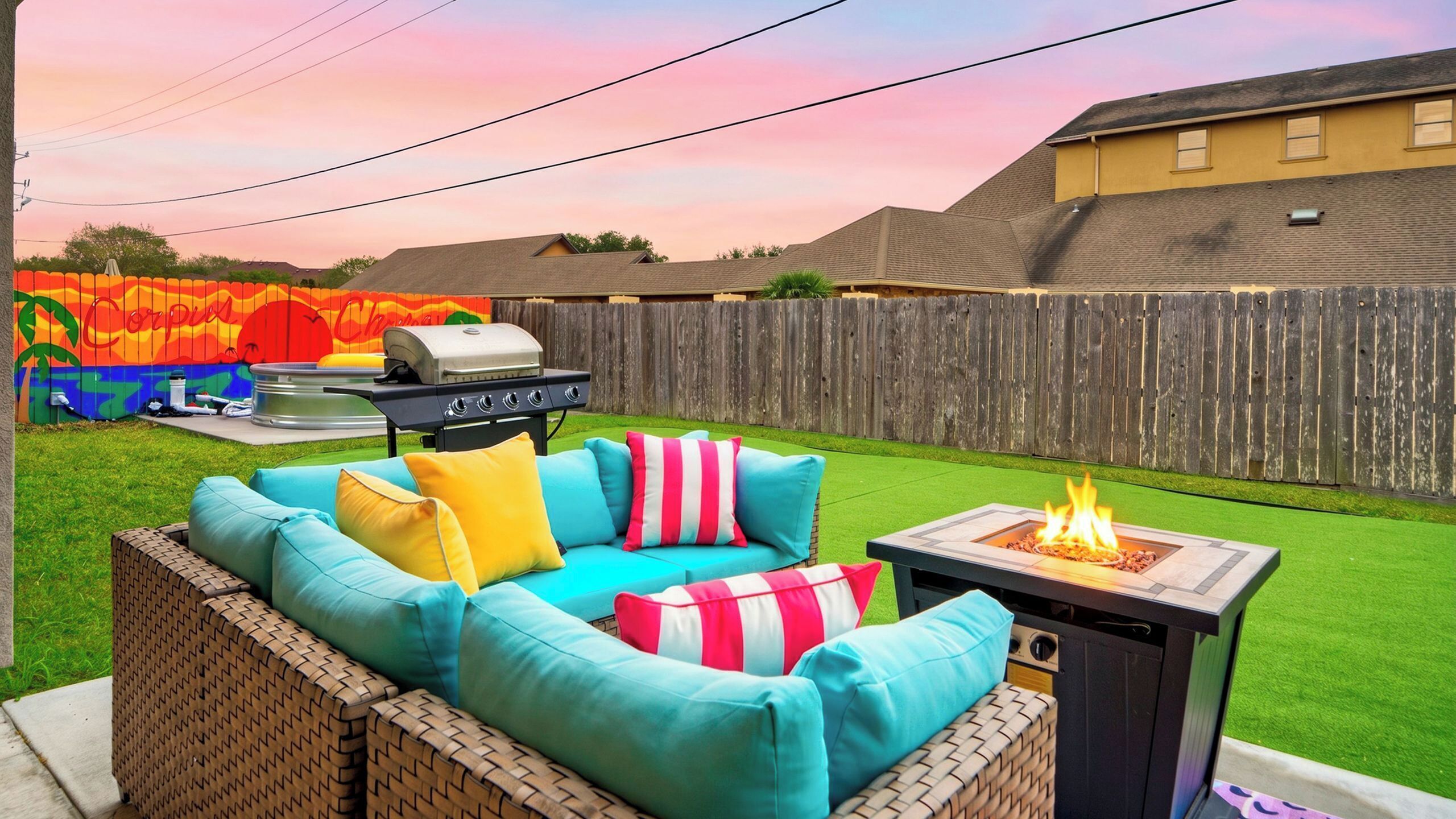 A backyard with a grill, a fire pit, and a colorful mural on the fence.