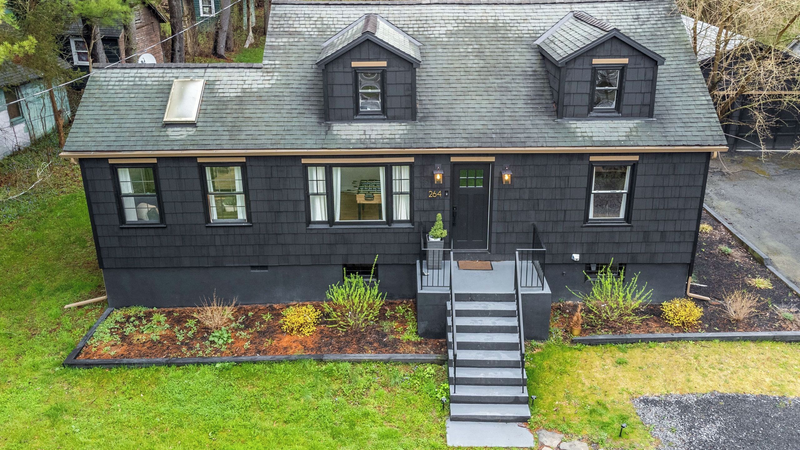 A two-story house with a dark exterior, a front door, and a staircase leading to the entrance.