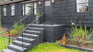 Una casa moderna con fachada oscura, una escalera de hormigón y un pequeño jardín con plantas.