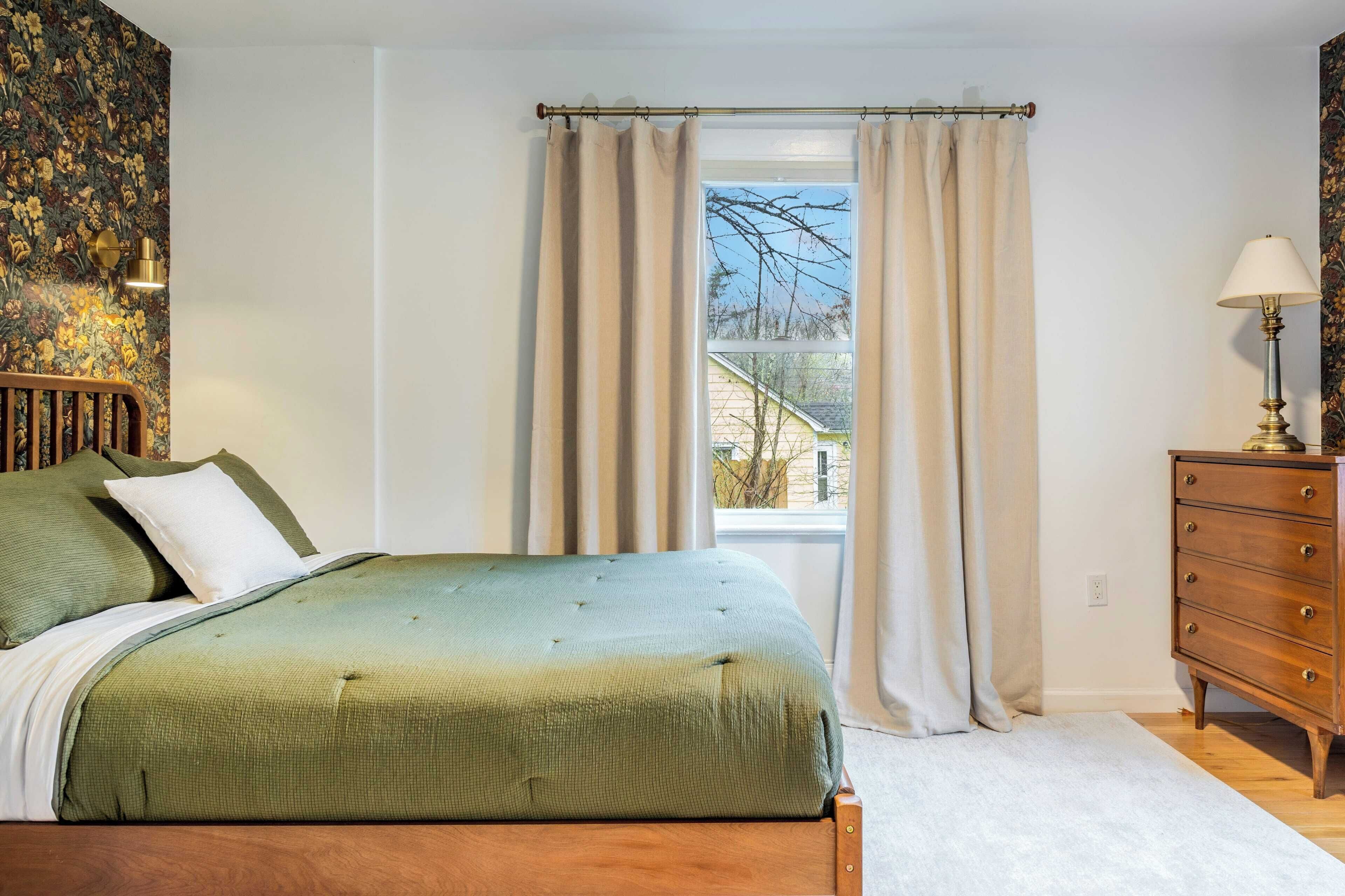 Quarto com cama, penteadeira, luminária e janela com cortinas.
