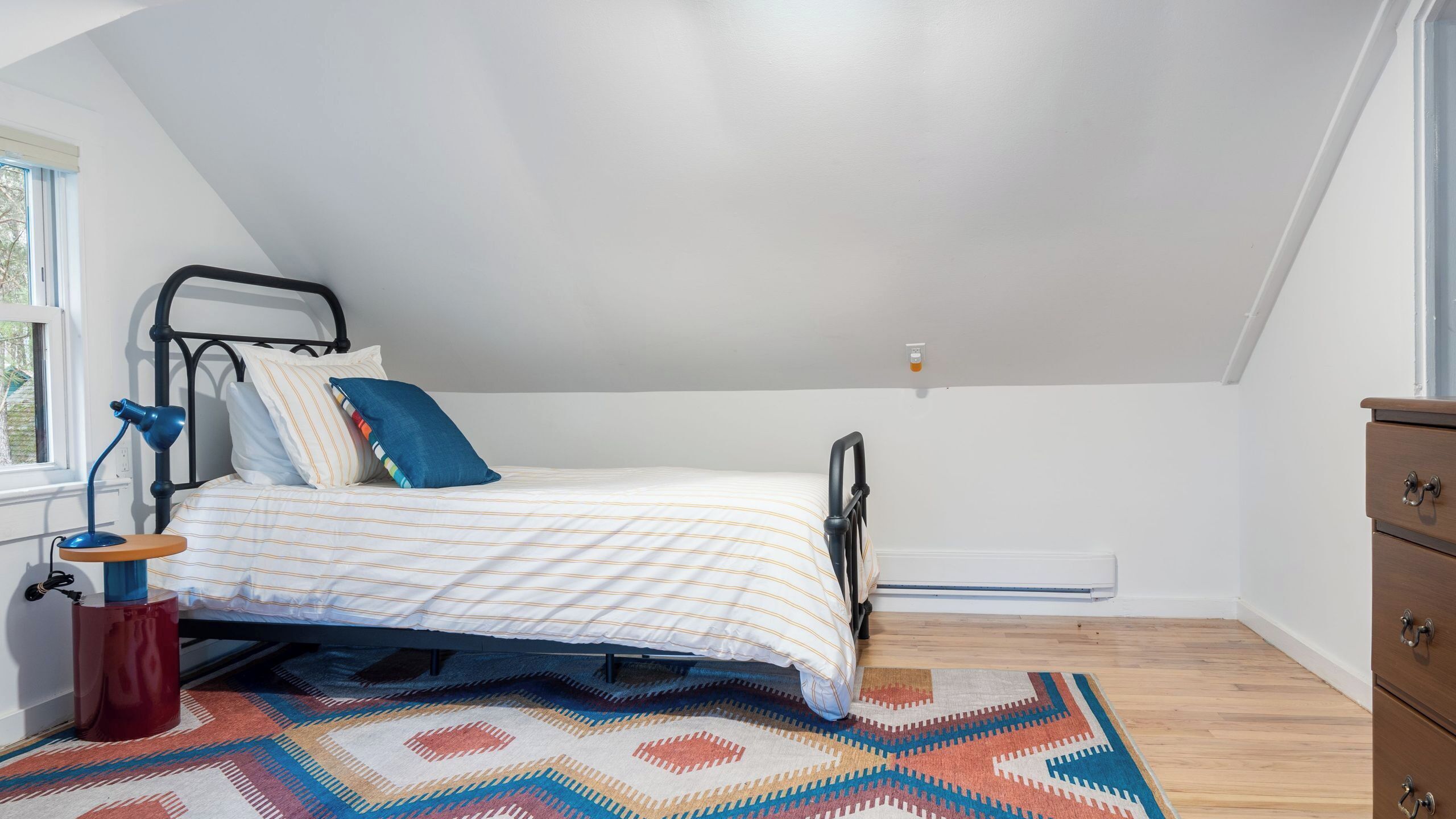 A bedroom with a bed, a desk, a chair, a window, and a radiator.