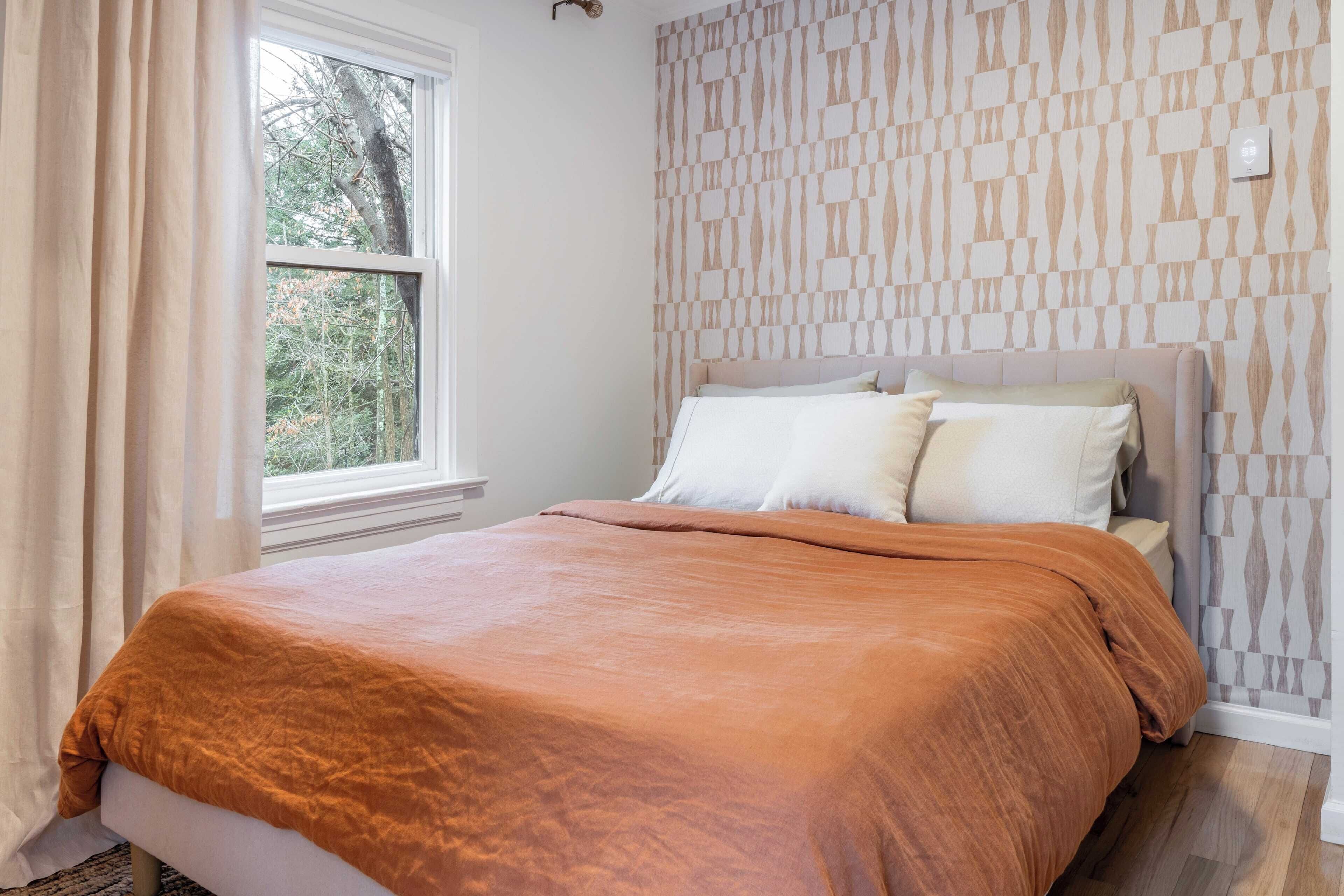 Ein Schlafzimmer mit Bett, Fenster und Wand mit Muster.