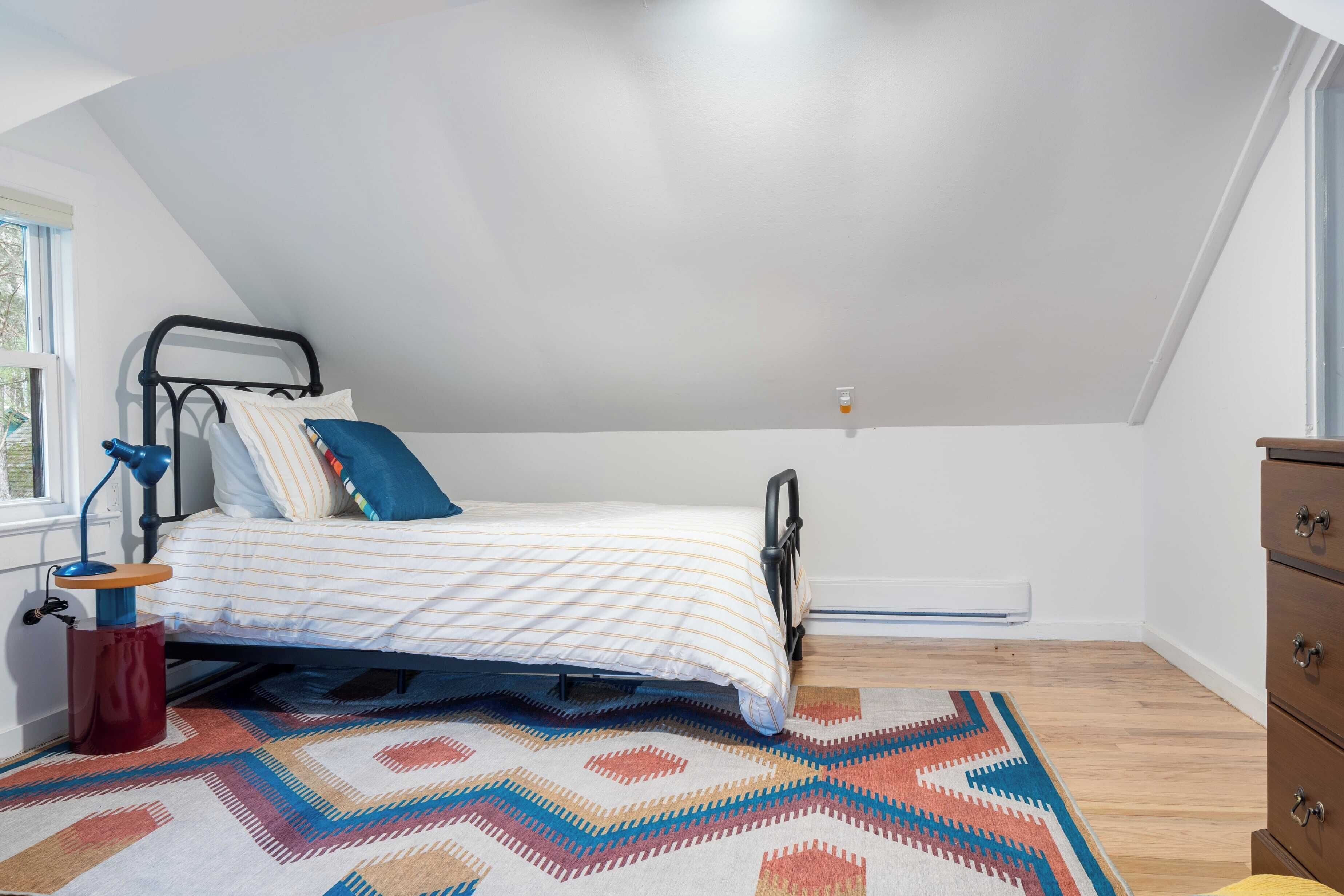 Une chambre à coucher avec un lit, un bureau, une chaise, une commode et une fenêtre.