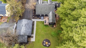An aerial view of a residential property with a paved driveway, a lawn, and a fire pit area.