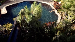 Zona de piscina con sillones de descanso y sombrillas, rodeada de exuberante vegetación y vista al mar.