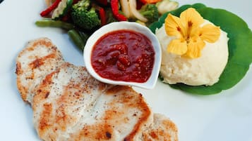 Une assiette blanche contenant du poulet grillé, une salade en accompagnement, de la purée de pommes de terre et une fleur en guise de décoration.