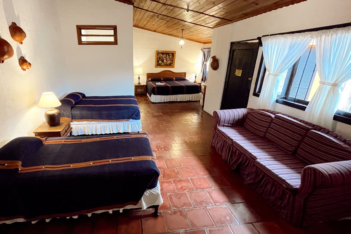 Habitación con dos camas, un sofá, una lámpara y una ventana con cortinas.