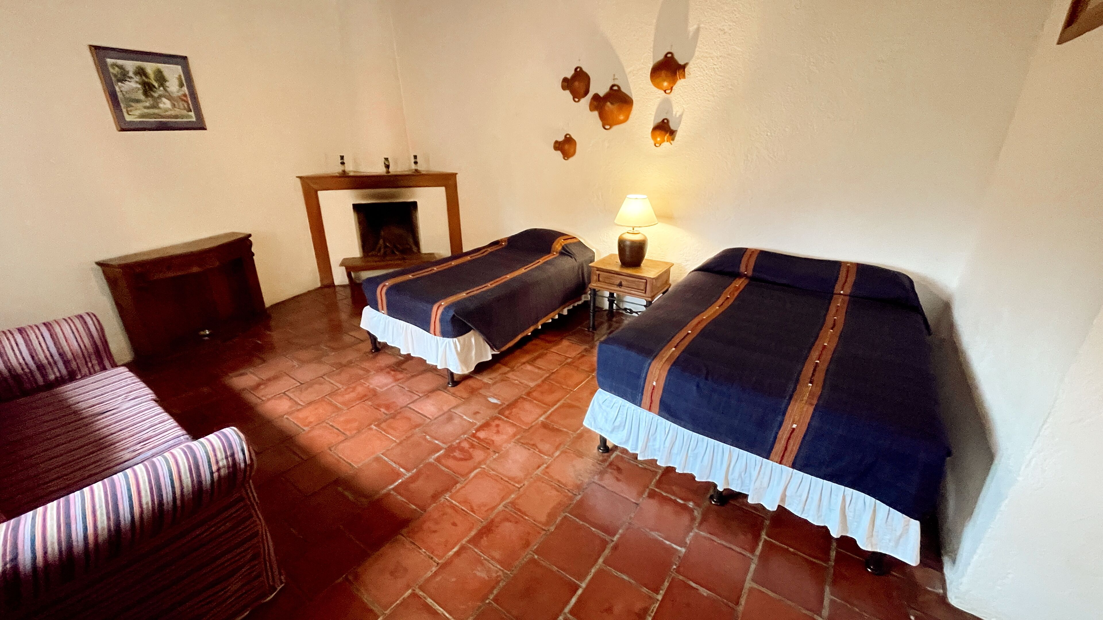 A room with two beds, a wooden chair, a small table, and a fireplace.