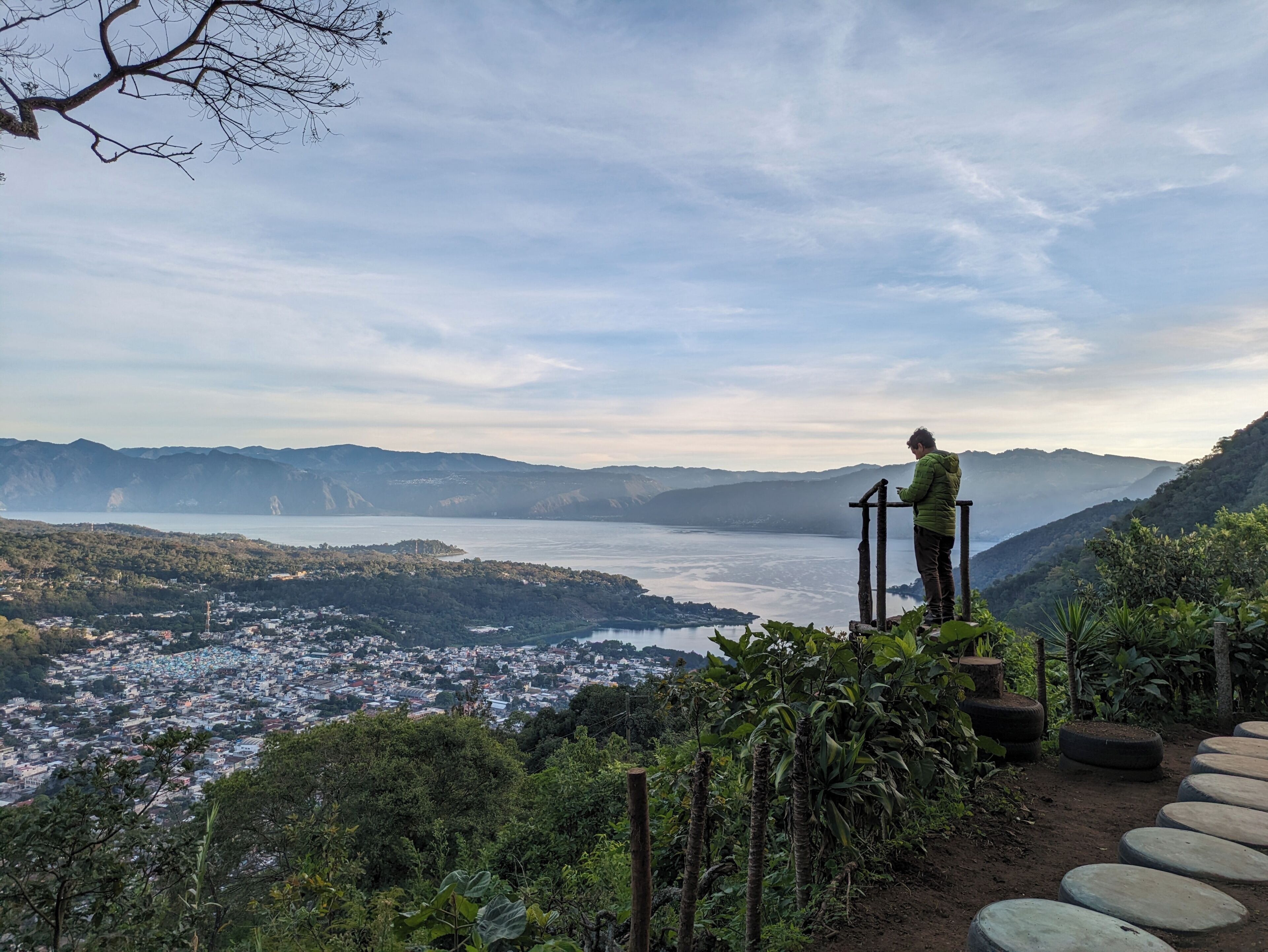 Une personne se tient sur une plateforme en bois, d’où elle a une vue panoramique sur une vallée, un lac et une ville situés en contrebas.
