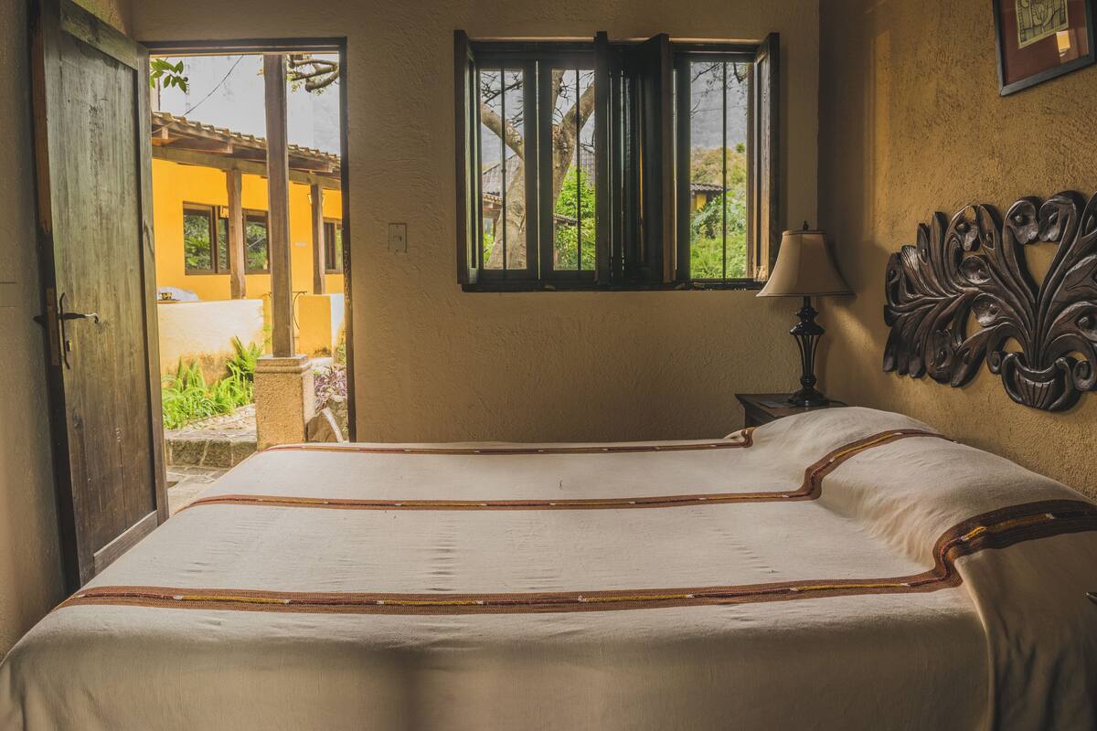 Un dormitorio con una cama grande, una ventana con rejas, una lámpara y un cabecero decorativo.