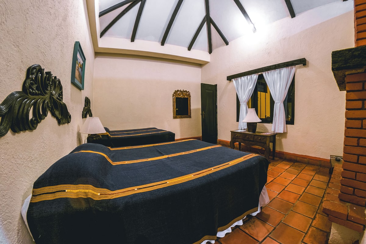 Una habitación con dos camas, cabecero de madera, un espejo, una mesita pequeña y una pared de ladrillo.