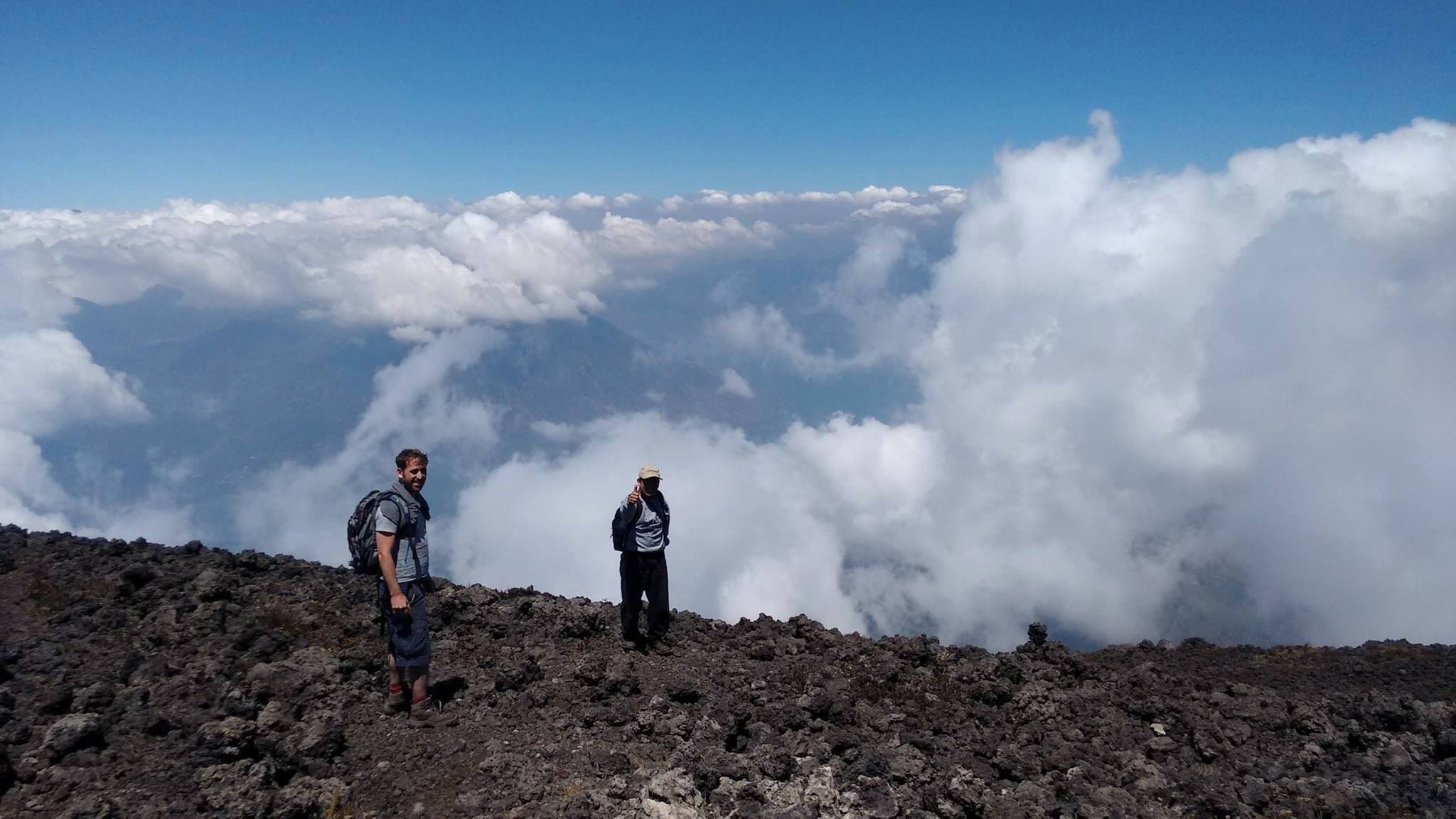 Deux personnes se tiennent sur un terrain rocheux, avec une vue sur les nuages en contrebas.