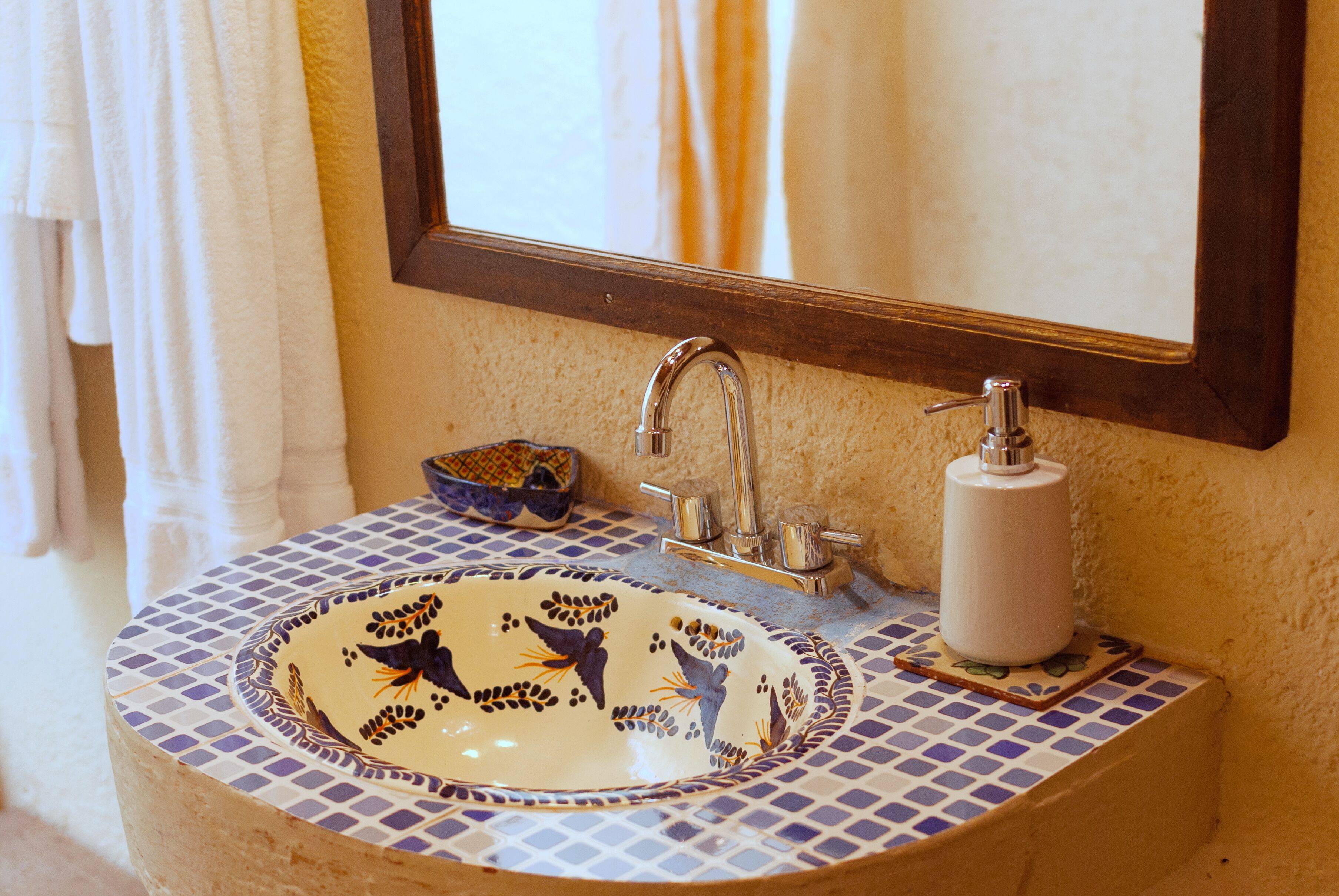 A bathroom sink with a mosaic tile design, a mirror, and a soap dispenser.