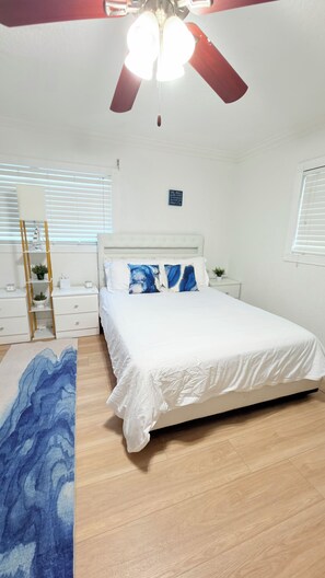 A bedroom with a bed, a nightstand, a dresser, a ceiling fan, and a window with blinds.